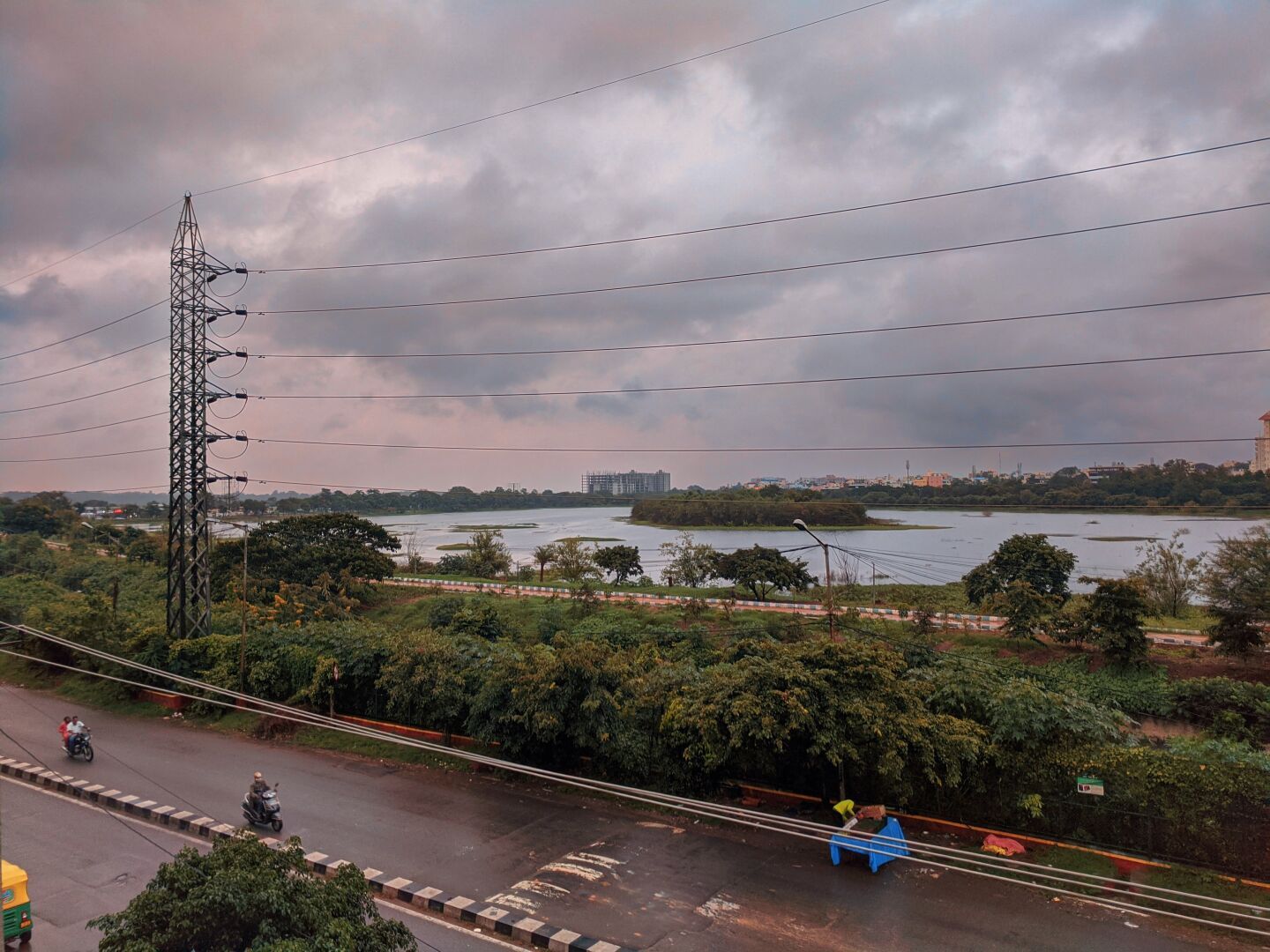 Photo of a lakeside after rain. A road beside the lake, wet from rain, sky covered with dark clouds, large electricity lines are visible.